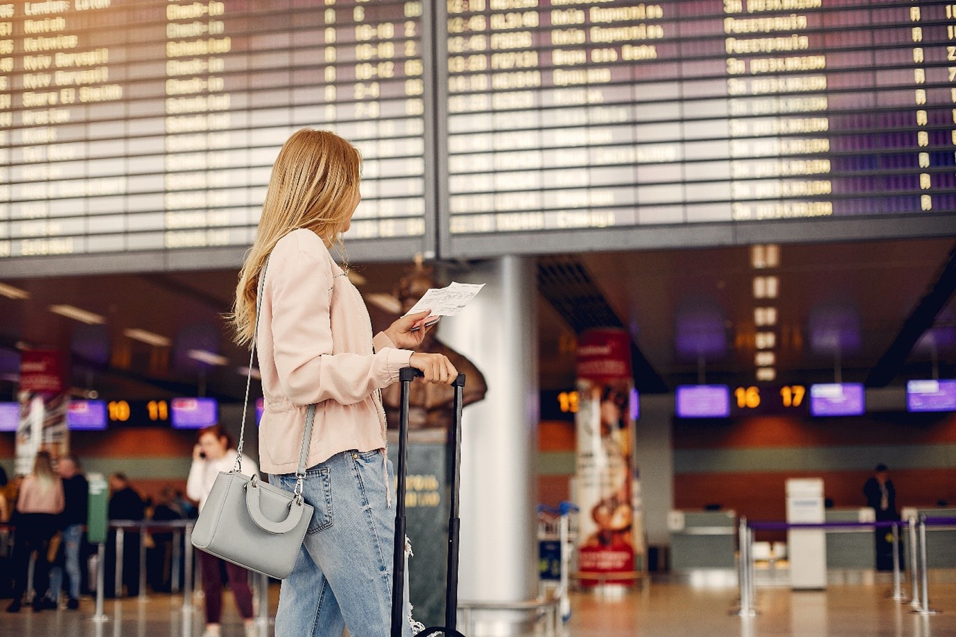 Passenger checking flight delay or cancellation details on the airport departure board with boarding pass and luggage